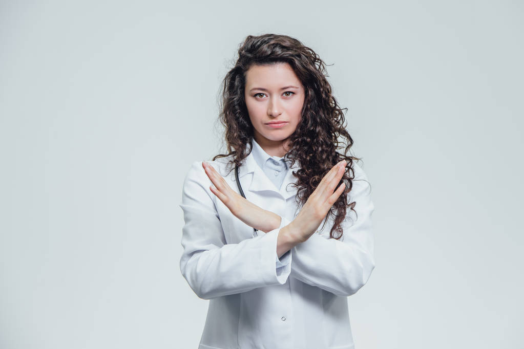 Молодой врач - девушка в белом халате. Руки шире, не показывая консенсуса. Стоя на сером фоне
. - Фото, изображение
