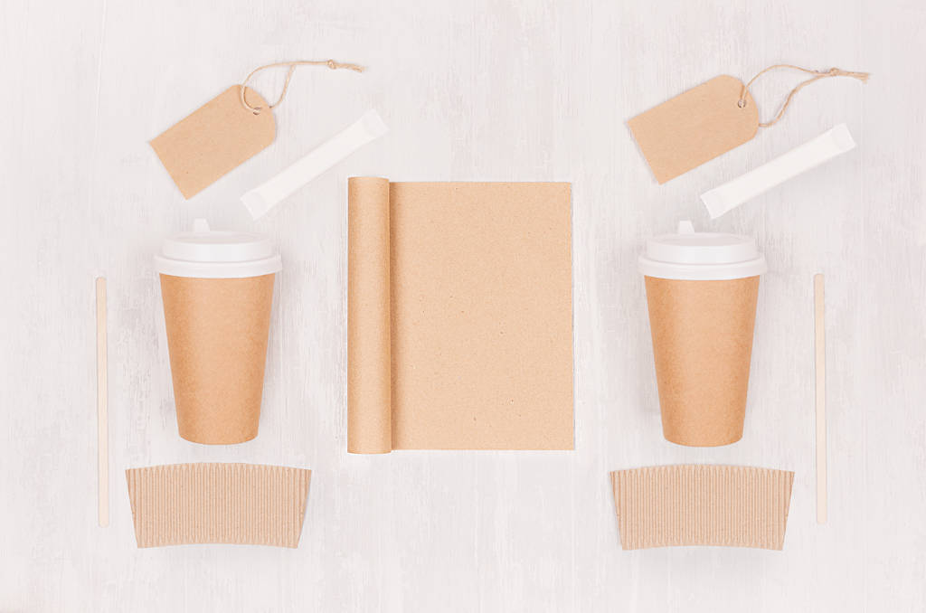 Шаблон кав'ярні для фірмового стилю: дві коричневі паперові чашки з чистим блокнотом, етикеткою, цукром на дошці з білого дерева, вид зверху
. - Фото, зображення
