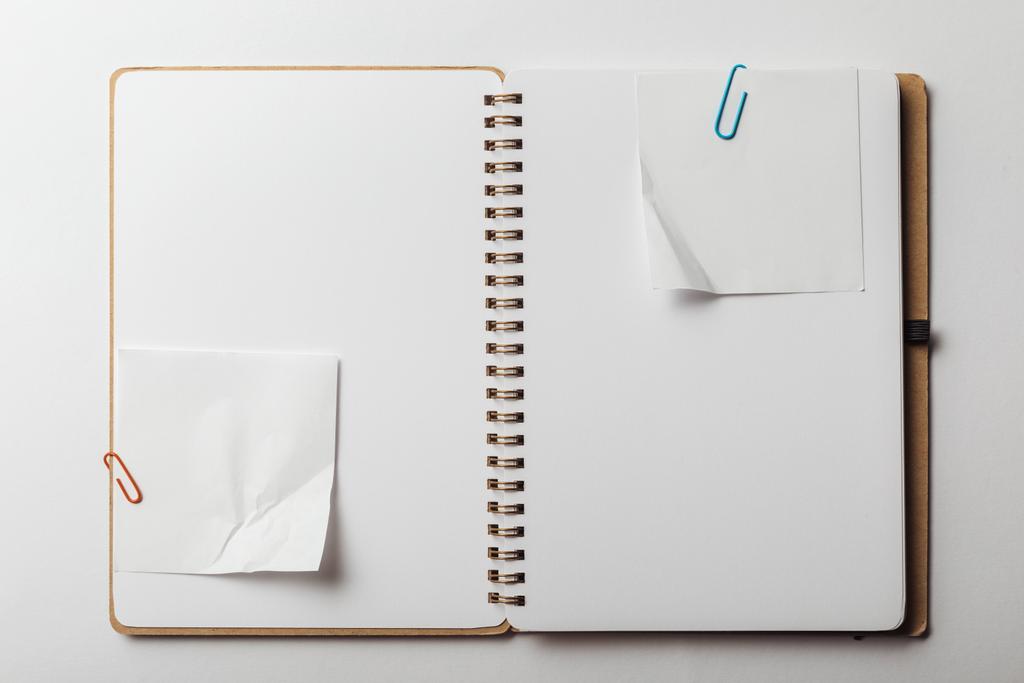 bovenaanzicht van laptop met kleverige nota's en paperclips op witte achtergrond - Foto, afbeelding
