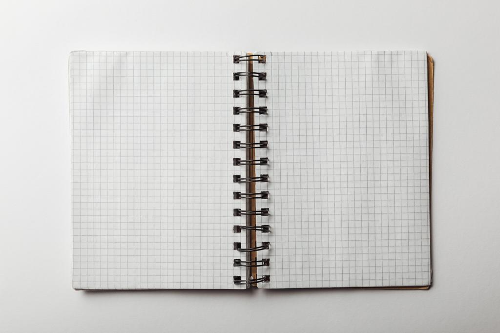 Draufsicht auf geöffnetes Notizbuch mit leeren quadratischen Papieren auf weißem Hintergrund - Foto, Bild