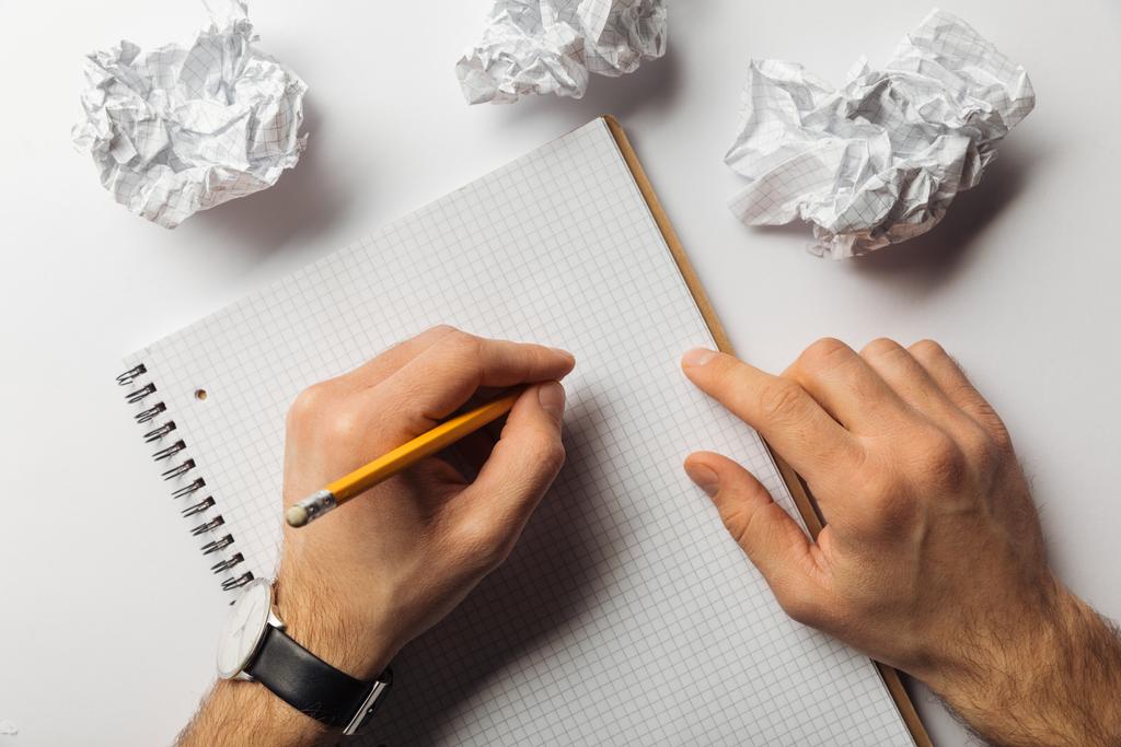 обрезанный вид человека, пишущего на пустом квадратном листе возле скомканных бумаг на белом фоне
  - Фото, изображение
