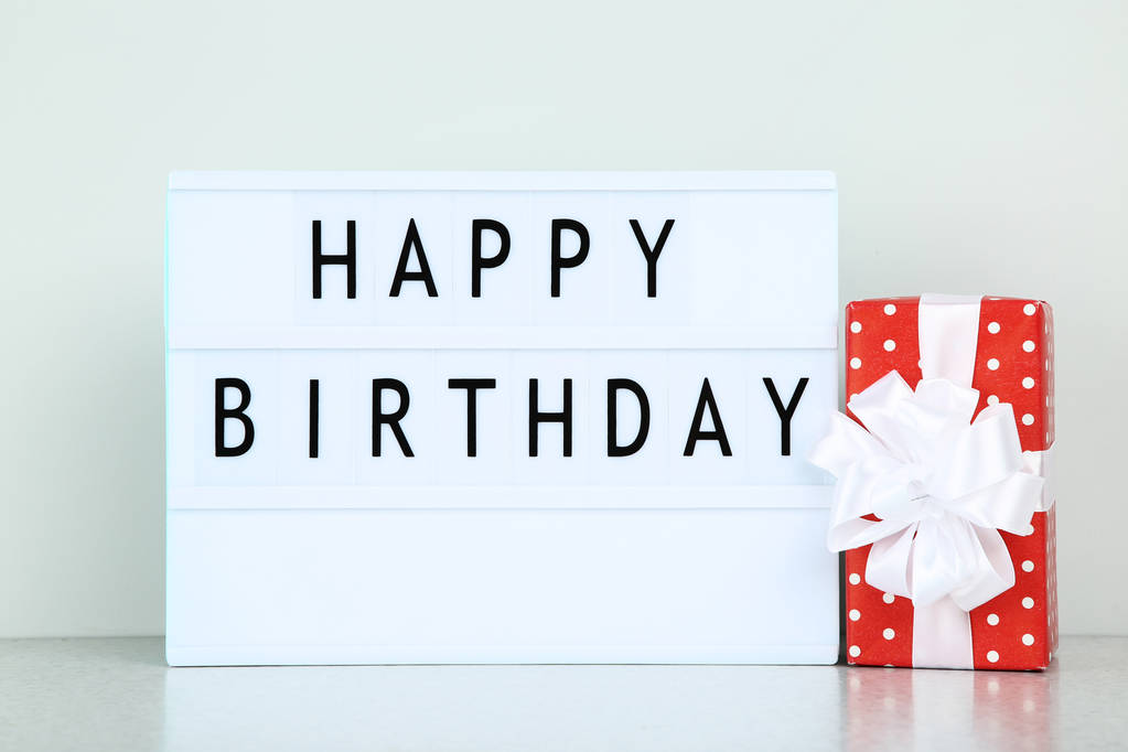 Leuchtkasten mit den Worten Happy Birthday und roter Geschenkbox auf grauem Hintergrund - Foto, Bild