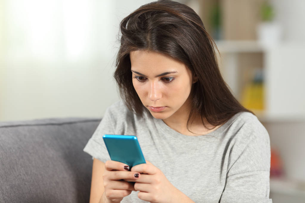 Addicted teen vérifier le contenu du téléphone intelligent assis sur un canapé dans le salon à la maison
 - Photo, image