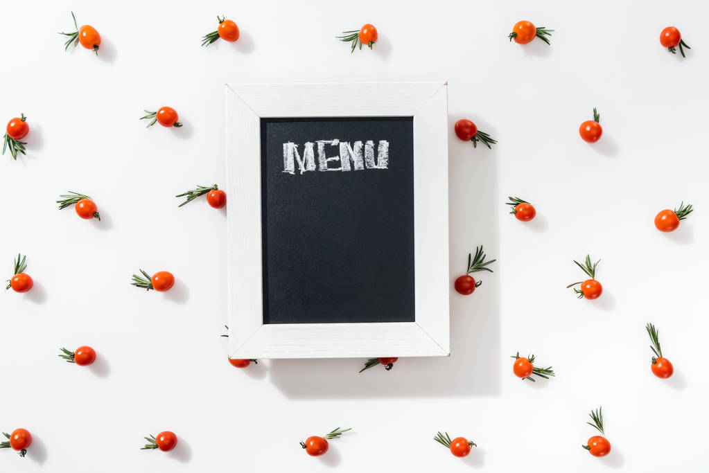 bovenaanzicht van krijt bord met menu belettering onder cherry tomaten en bladeren  - Foto, afbeelding