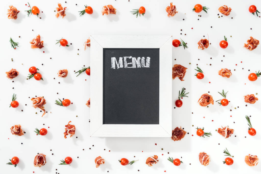 Kreidetafel mit Menüaufdruck zwischen Tomaten, Prosciutto, Gewürzen und Blättern  - Foto, Bild