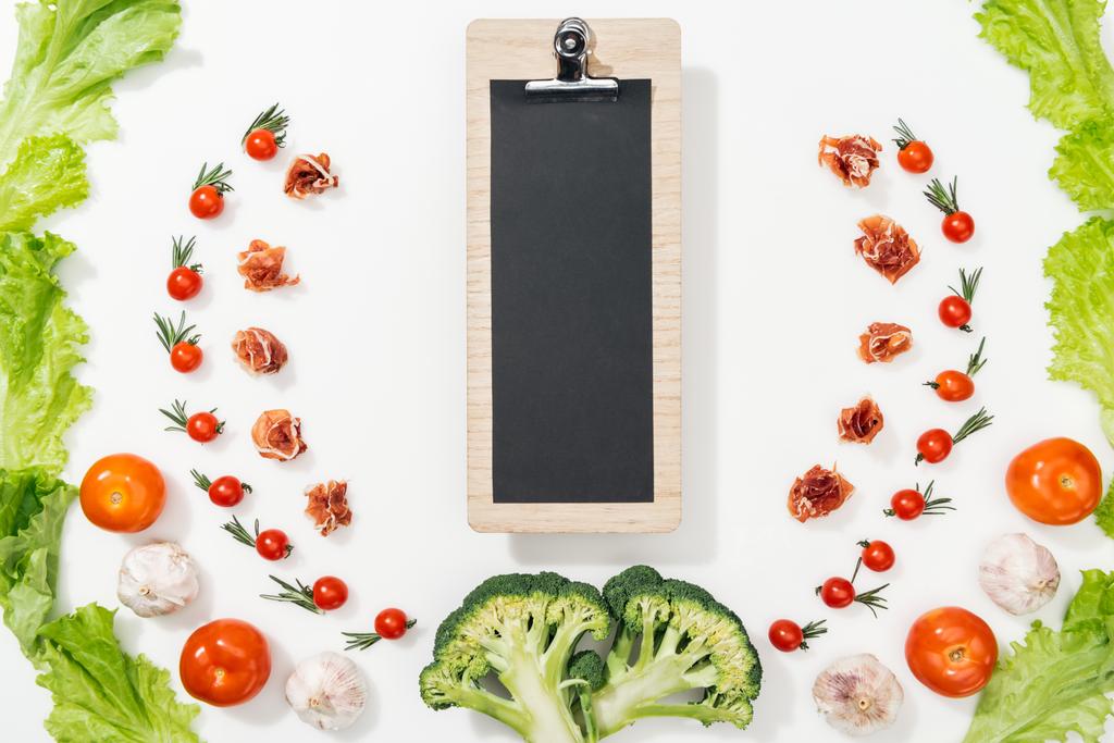 top view of clipboard among tomatoes, lettuce leaves, prosciutto, broccoli and garlic - Photo, Image