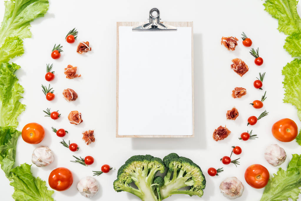 top view of white clipboard among tomatoes, lettuce leaves, prosciutto, broccoli and garlic - Photo, Image