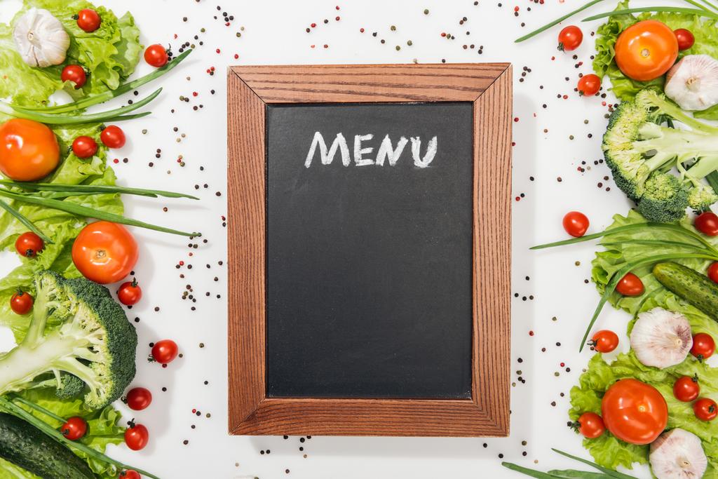 vista superior de pizarra con letras de menú entre tomates, hojas de lechuga, pepinos, cebolla, especias y ajo
 - Foto, Imagen