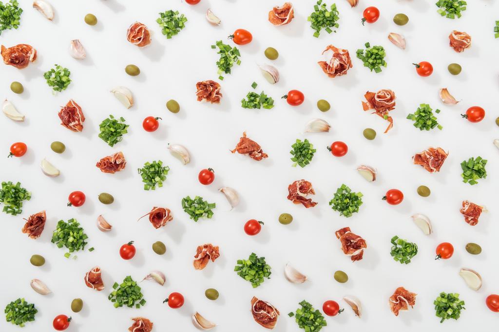 bovenaanzicht van prosciutto, olijven, knoflookteentjes, groen en kerstomaatjes - Foto, afbeelding