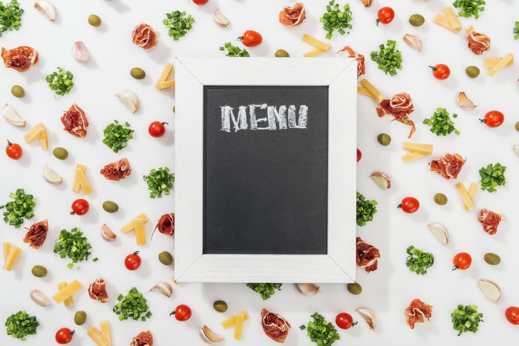 bovenaanzicht van krijt bord met menu belettering onder olijven, prosciutto, groen, gesneden kaas, knoflookteentjes en kerstomaatjes - Foto, afbeelding