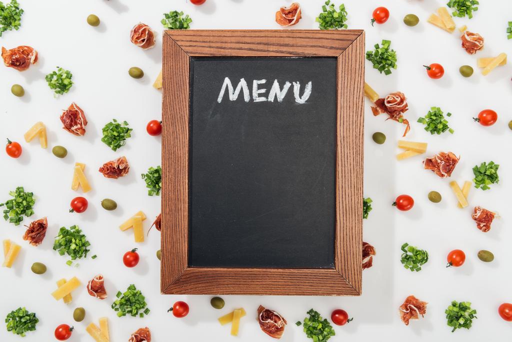 top view of chalk board with menu lettering among olives, prosciutto, greenery, cut cheese and cherry tomatoes - Photo, Image