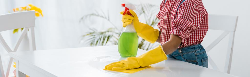 niño afroamericano con la tabla verde de la limpieza de la botella del aerosol en guantes de goma amarillos
 - Foto, imagen