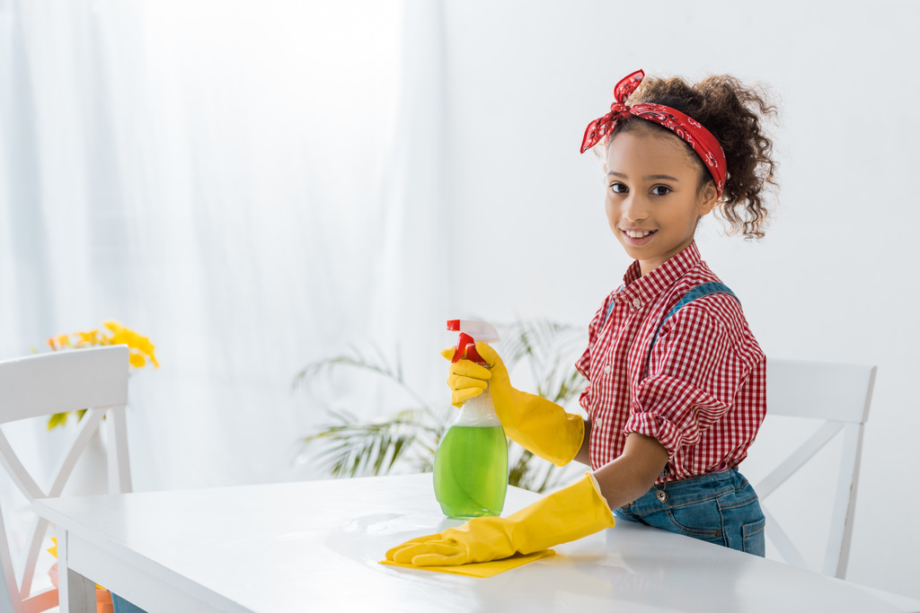 cute african american child in plaid shirt cleaning table in yellow rubber gloves - Photo, Image