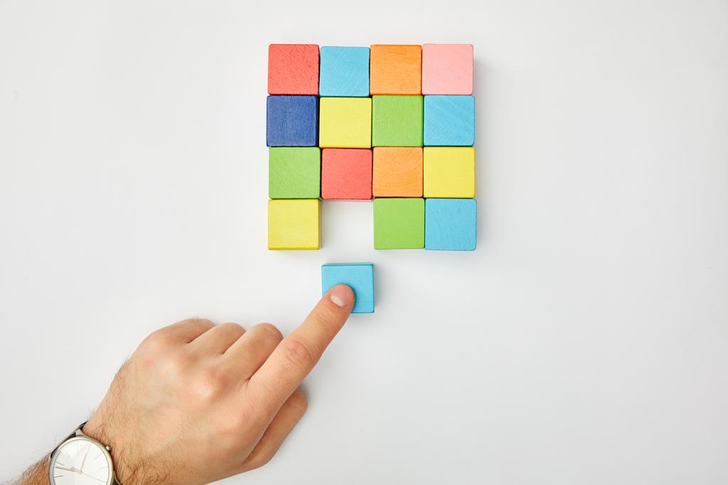 περικοπεί θέα αρσενική χέρι βάζοντας κύβου σε σύνολο από πολύχρωμα τετράγωνα σε γκρίζο φόντο - Φωτογραφία, εικόνα