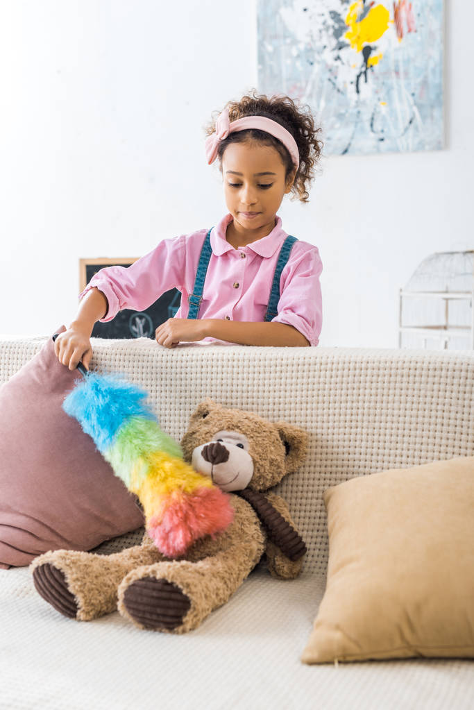adorable african american child cleaning teddy bear with colorful duster - Photo, Image