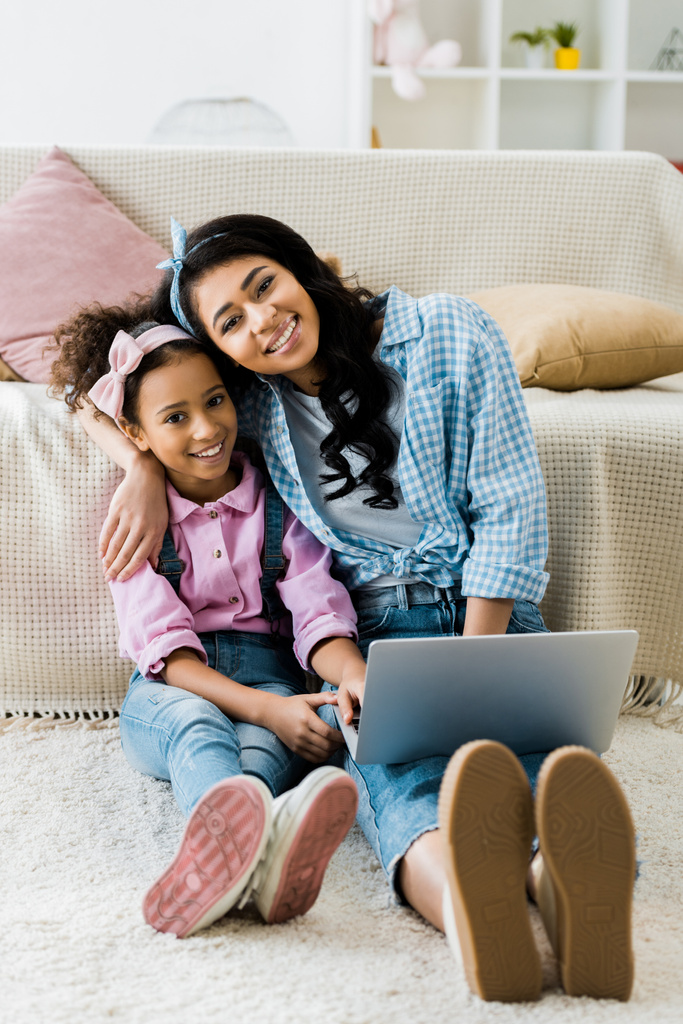 笑顔のアフリカ系アメリカ人の母と娘カーペット ソファーのそばに座ってラップトップを使用して - 写真・画像