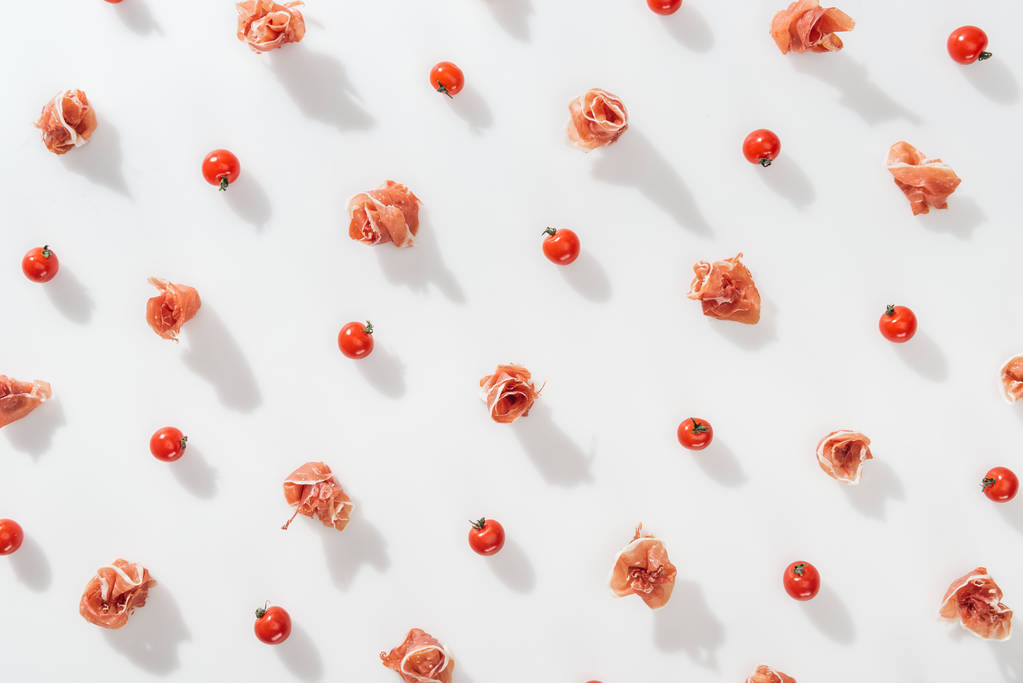 Draufsicht auf schmackhaften Prosciutto in der Nähe von roten Kirschtomaten auf weißem Hintergrund - Foto, Bild