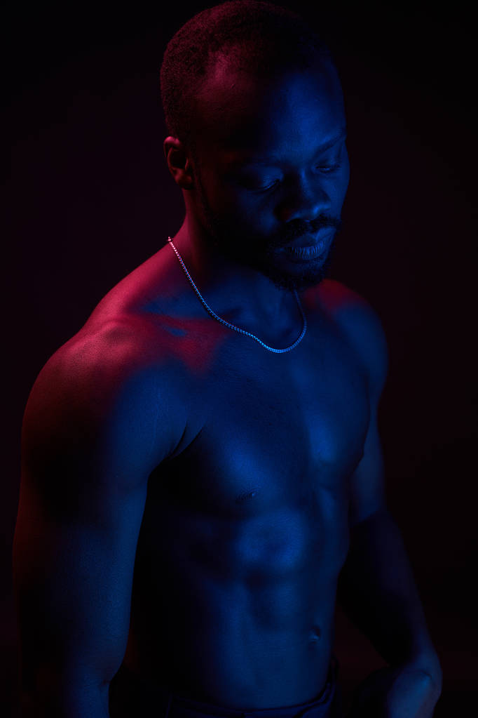 Червоно-синій освітлений портрет молодого і сексуального м'язистого чоловіка без сорочки з ланцюжком шиї
.  - Фото, зображення