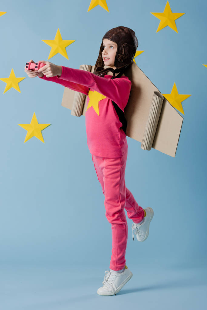 Oyun çubuğu mavi yıldızlı arka plan üzerinde tutarak uçuş kask içinde taşımak çocuk - Fotoğraf, Görsel