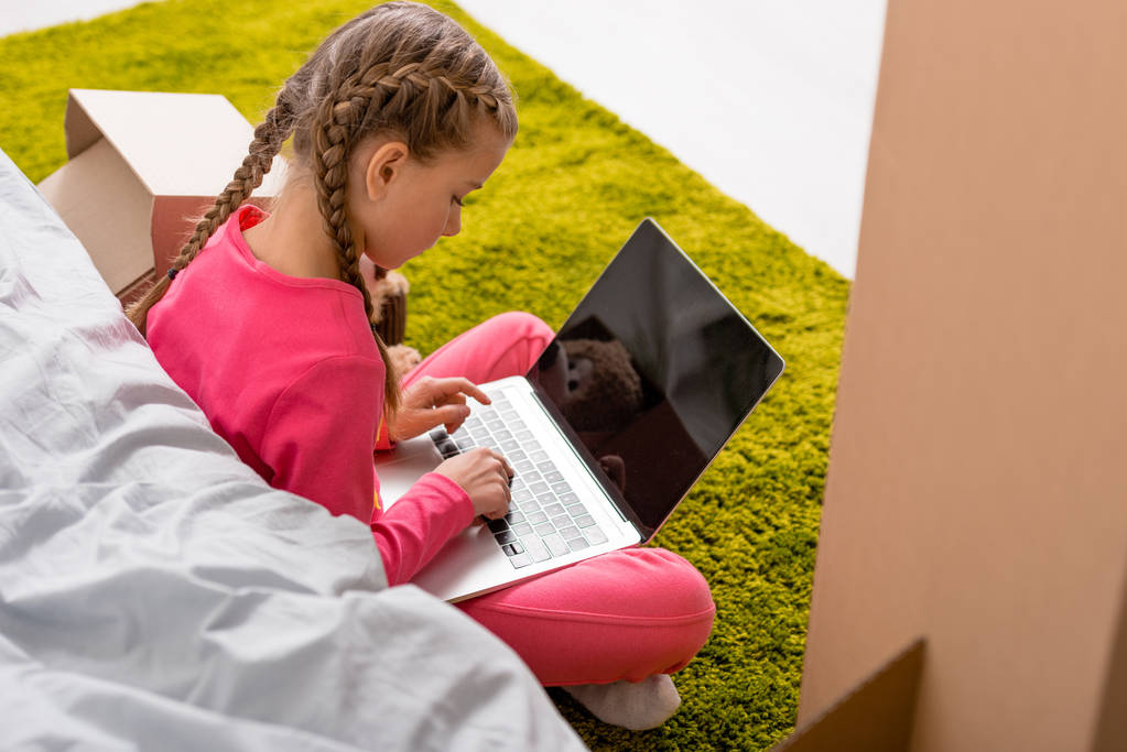 Enfant avec des tresses assis sur le tapis et tapant sur le clavier de l'ordinateur portable
 - Photo, image