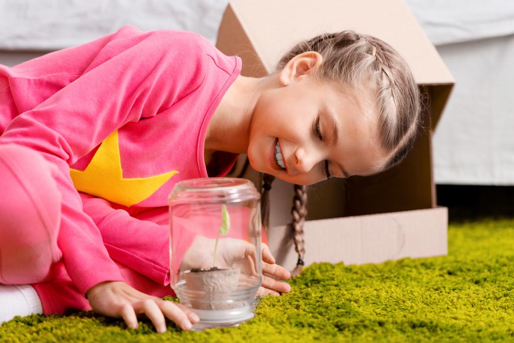 Enfant souriant regardant la plante dans un bocal en verre avec intérêt
 - Photo, image