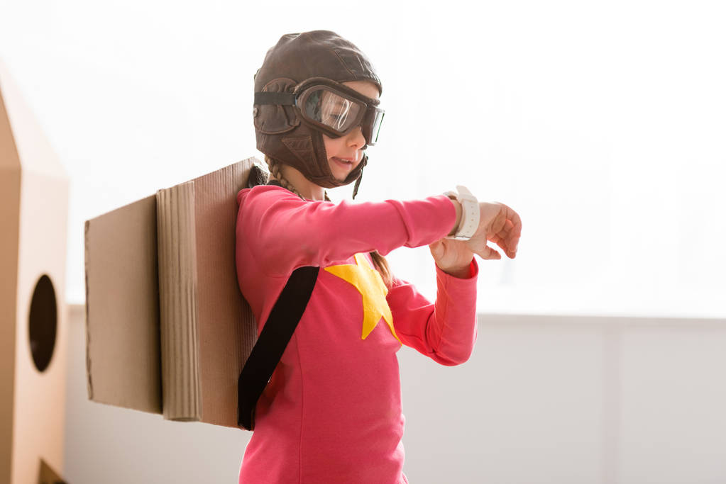 Kind in vlucht helm en bril kijken horloge - Foto, afbeelding