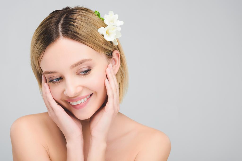 attractive smiling girl with perfect skin and freesia flowers in hair, isolated on grey - Photo, Image