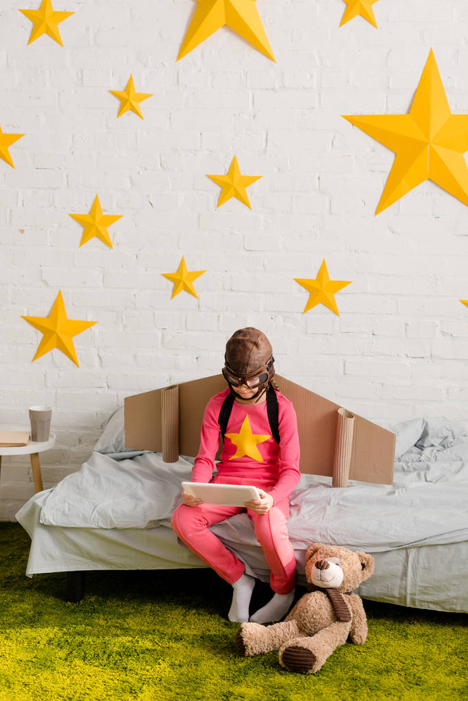 Ребенок в летном шлеме сидит на кровати и с помощью цифрового планшета
 - Фото, изображение