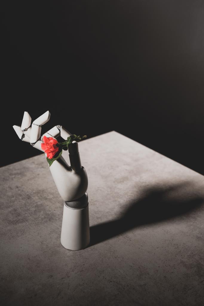 rosa Rose Blume in Roboterhand auf Steintisch auf schwarzem Hintergrund - Foto, Bild