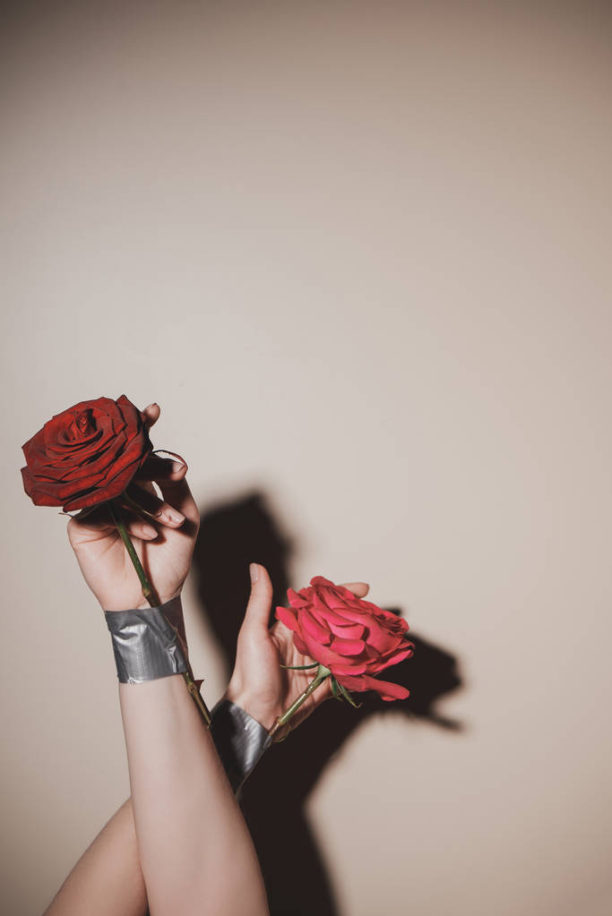 Teilansicht einer Frau mit getapten roten Rosenblüten auf beigem Hintergrund - Foto, Bild