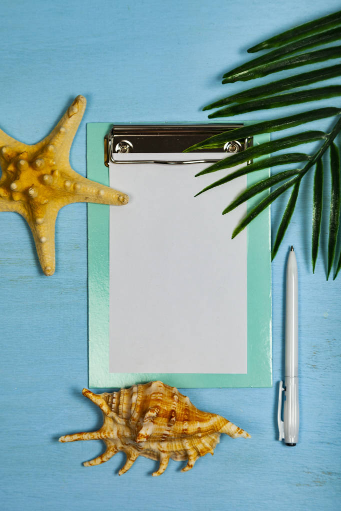 Planeia uma viagem ao mar. Papel, conchas, estrelas do mar e folha de palmeira sobre um fundo de madeira azul
. - Foto, Imagem