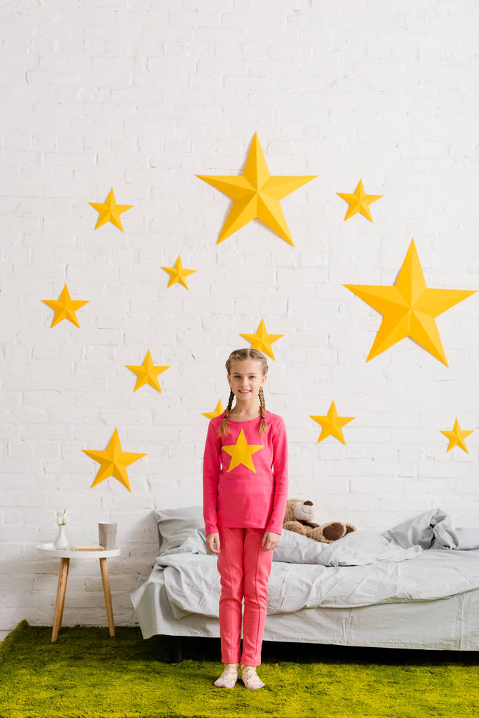 Cheerful kid in pink clothes standing in front of bed - Photo, Image