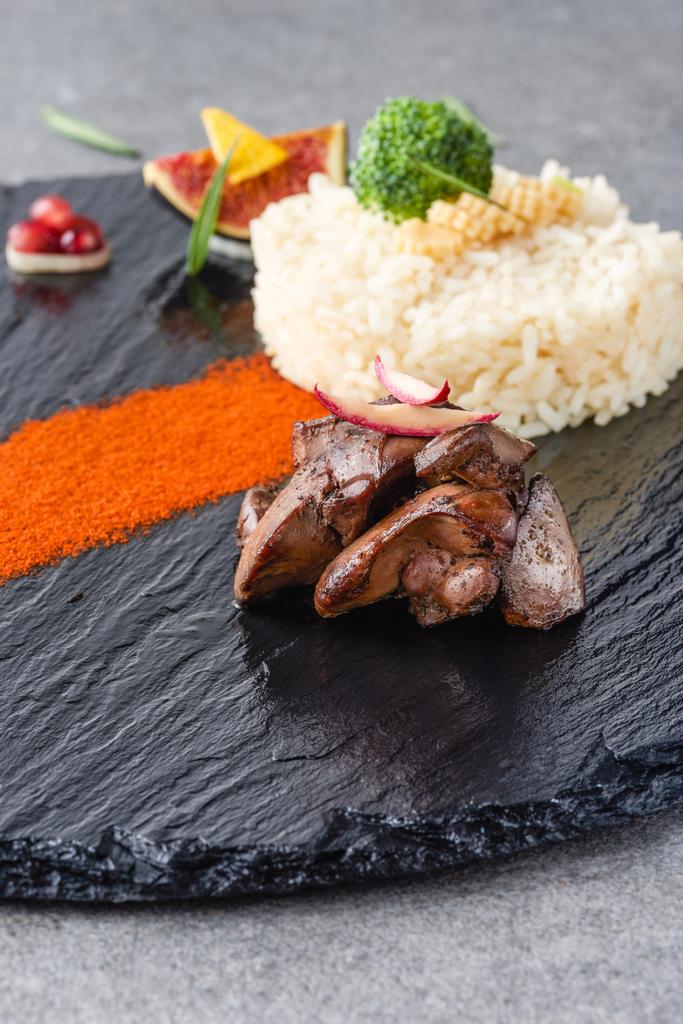 rýže, brokolice, fíkovníky a smažené maso na černém plátu a kamenný povrch  - Fotografie, Obrázek