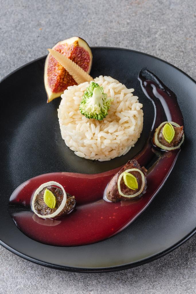 arroz, brócoli, higo y carne frita con salsa en plato negro y superficie de piedra
  - Foto, imagen
