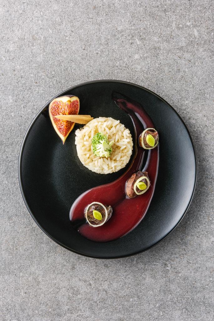 ylhäältä riisiä, parsakaalia, viikunaa ja paistettua lihaa kastikkeella mustalla lautasella
  - Valokuva, kuva