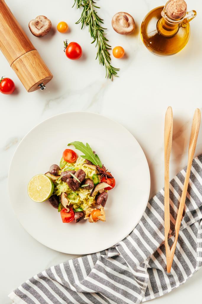 bovenaanzicht van salade op wit bord met fles olie, cherry tomaten en rozemarijn - Foto, afbeelding