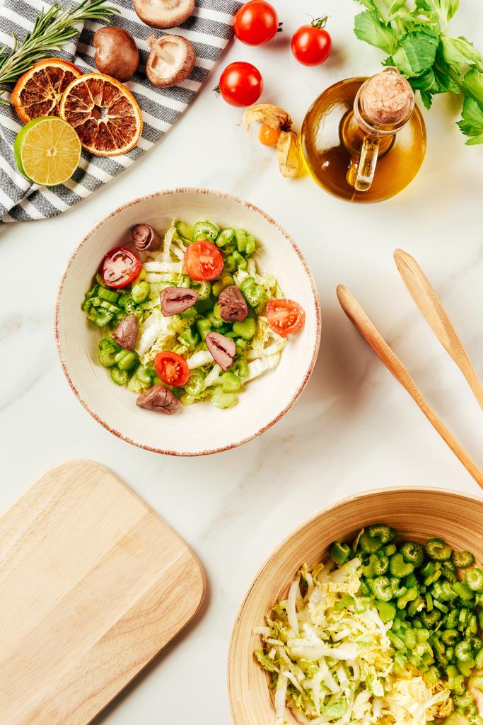 vue de dessus de salade, chou et céleri dans des bols avec bouteille d'huile, tomates cerises, citron vert et champignons
  - Photo, image