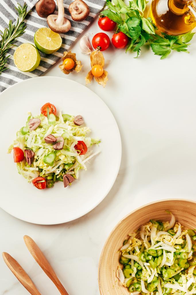 salade, chou et céleri dans une assiette avec bouteille d'huile, tomates cerises, citron vert et champignons
  - Photo, image
