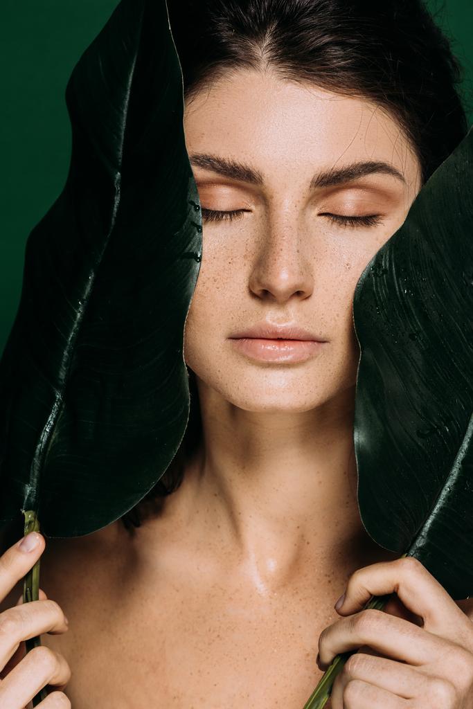 Πορτρέτο του όμορφη κοπέλα με κλειστά τα μάτια, ποζάρει με φύλλα που απομονώνονται σε πράσινο - Φωτογραφία, εικόνα