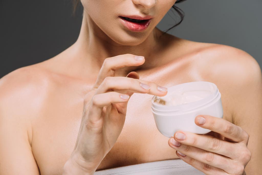 cropped view of woman holding plastic container with face cream isolated on grey - Photo, Image