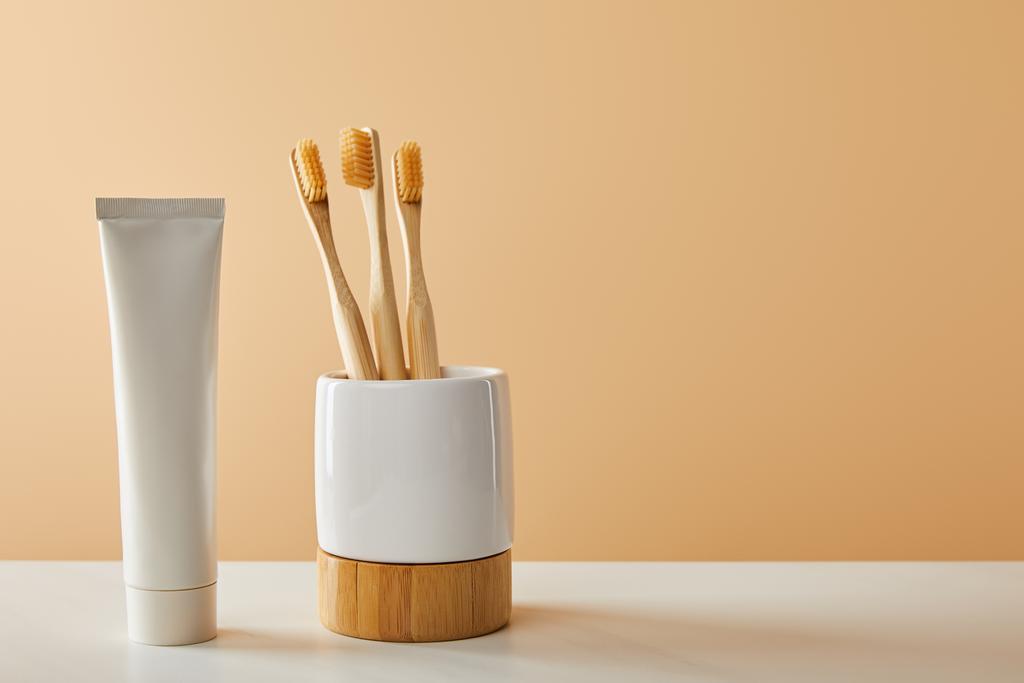 bamboo toothbrushes in holder and toothpaste in tube on white table and beige background - Photo, Image