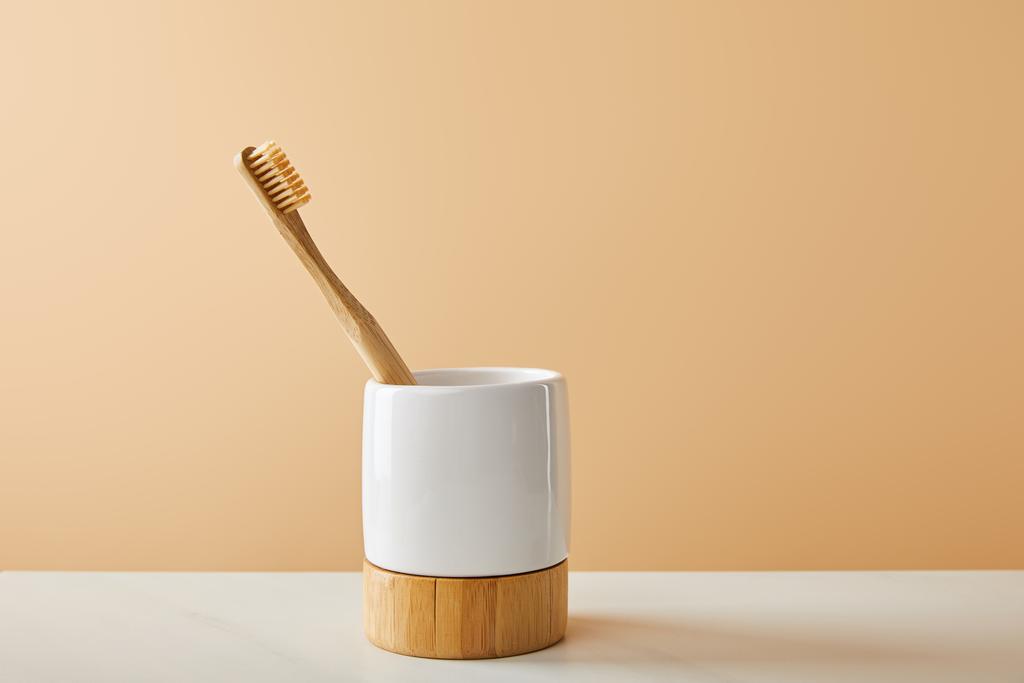 Bambus-Zahnbürste im Halter auf weißem Tisch und beigem Hintergrund - Foto, Bild