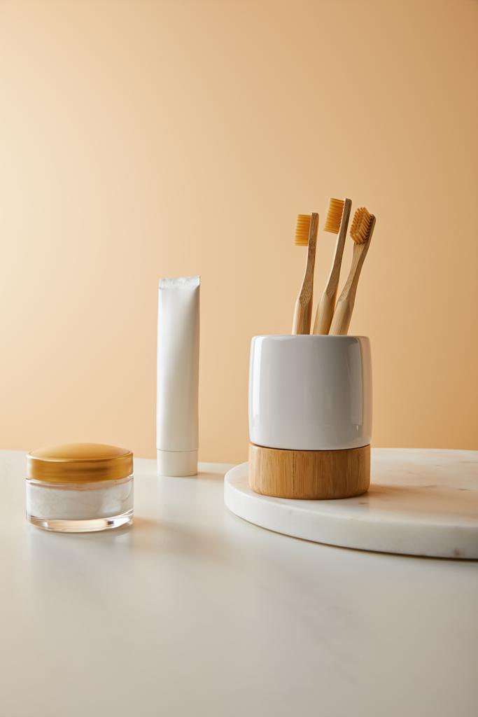 support avec brosses à dents sur plaque ronde en marbre, dentifrice en tube et crème cosmétique sur table blanche et fond beige
 - Photo, image