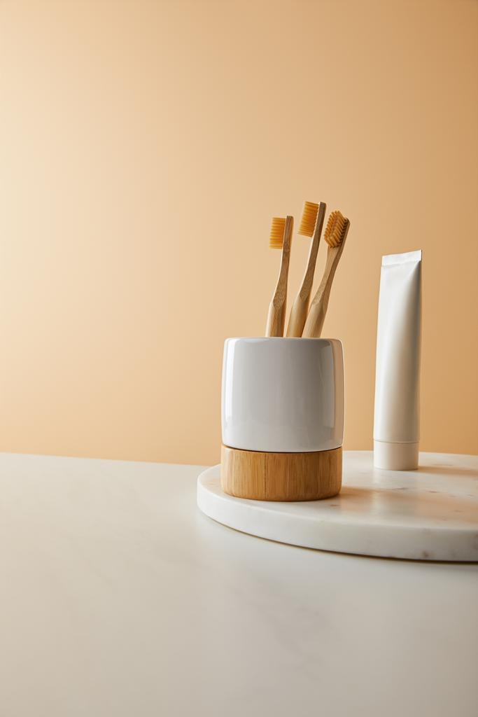 panneau rond en marbre avec dentifrice en tube et brosses à dents en bambou en support sur table blanche et fond beige
 - Photo, image