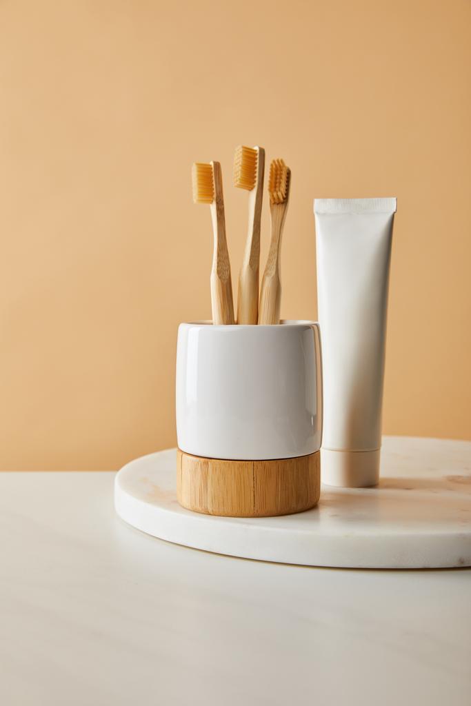 pasta de dentes em tubo e suporte com escovas de bambu na superfície de mármore branco e fundo bege
 - Foto, Imagem