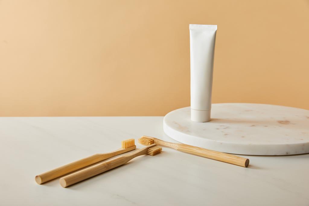 мраморная круглая доска с зубной пастой в тюбике и бамбуковыми зубными щетками на белом столе и бежевом фоне
 - Фото, изображение
