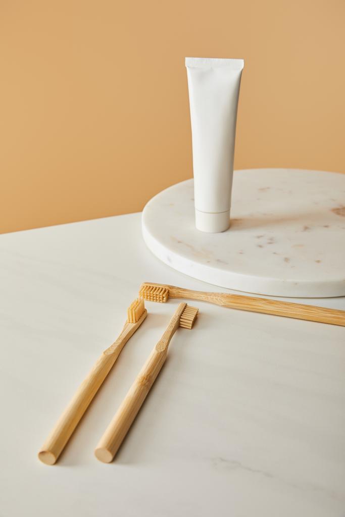 placa redonda de mármore com pasta de dentes em tubo e escovas de bambu na mesa branca e fundo bege
 - Foto, Imagem
