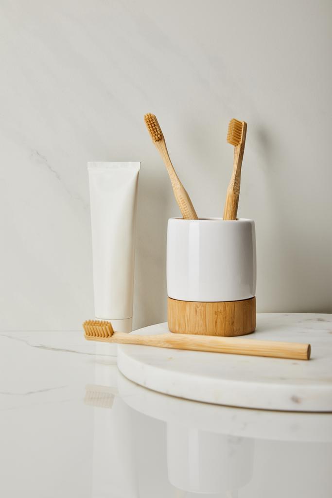 držák, bambusové kartáčky a zubní pastu v tubě na bílém mramorovém pozadí - Fotografie, Obrázek