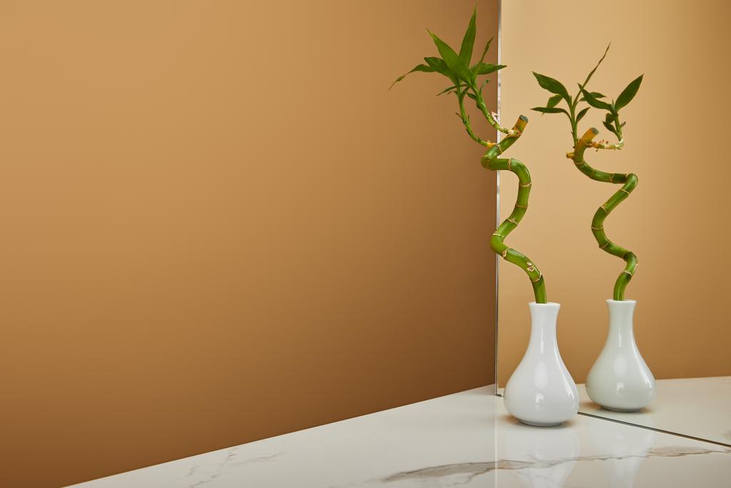 groene bamboe stam in vaas en spiegel op witte marmeren tafel en beige achtergrond - Foto, afbeelding