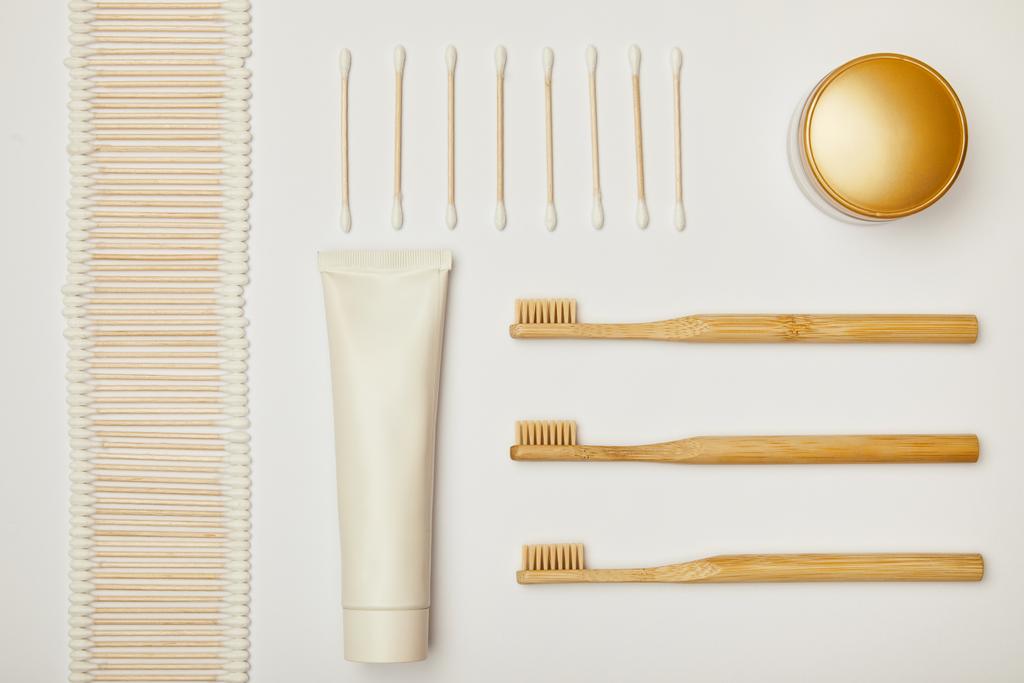 vista superior de paus de orelha dispostos, pasta de dentes em tubo, creme cosmético e escovas de dentes no fundo branco
 - Foto, Imagem